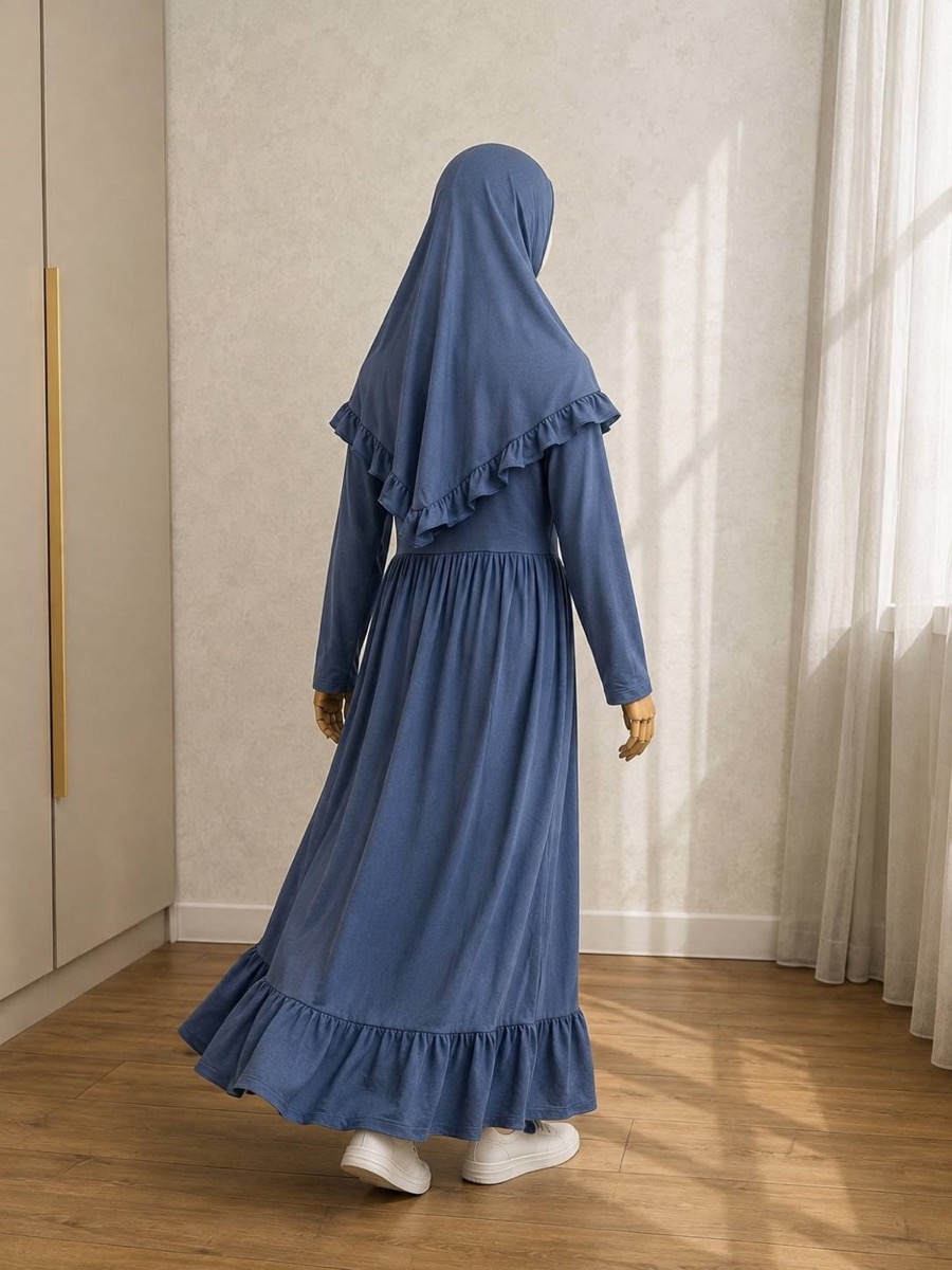 Girl's long blue dress with a matching ruffled khimar, photographed from the back in a sunlit studio