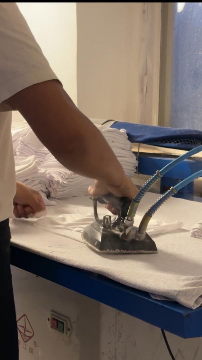 Steam iron pressing a white garment on a pressing table